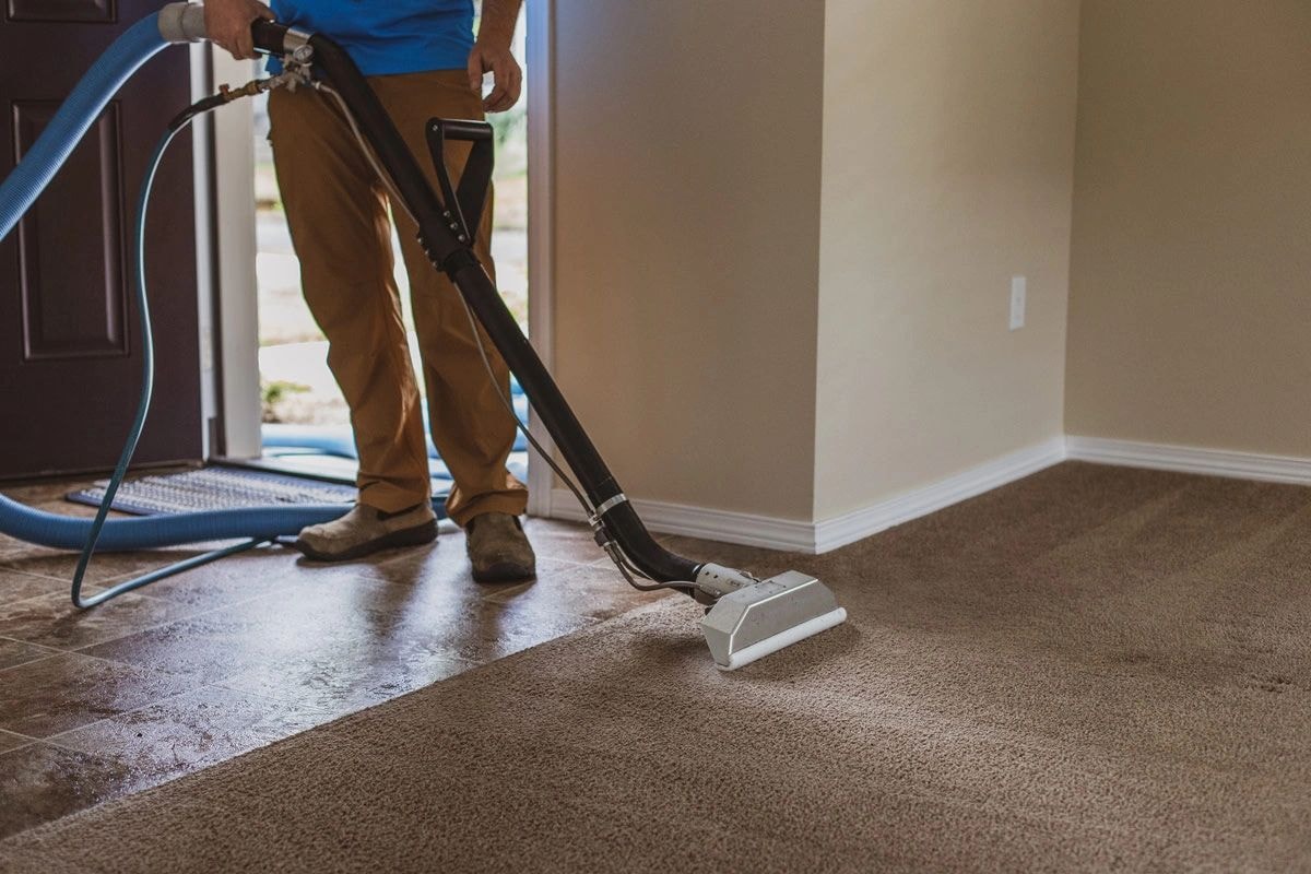 Professional carpet cleaning technician using a hot water extraction wand on residential carpet